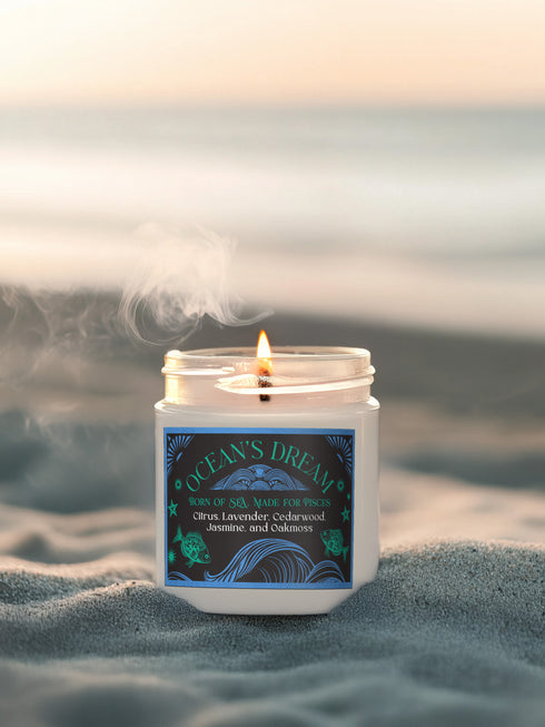 A 9 oz white soy candle in clear glass jar with blue and turquoise oceanic label featuring wave patterns and fish motifs, titled "Ocean's Dream" with a lit cotton wick.